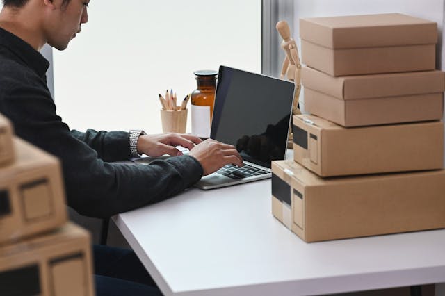 man sitting by a desk with boxes next to computer